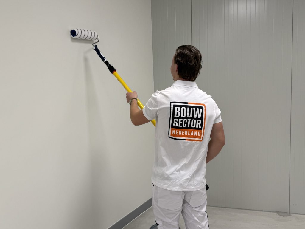 Schilder van Bouwsector Nederland rolt een witte wand met een roller aan een gele steel