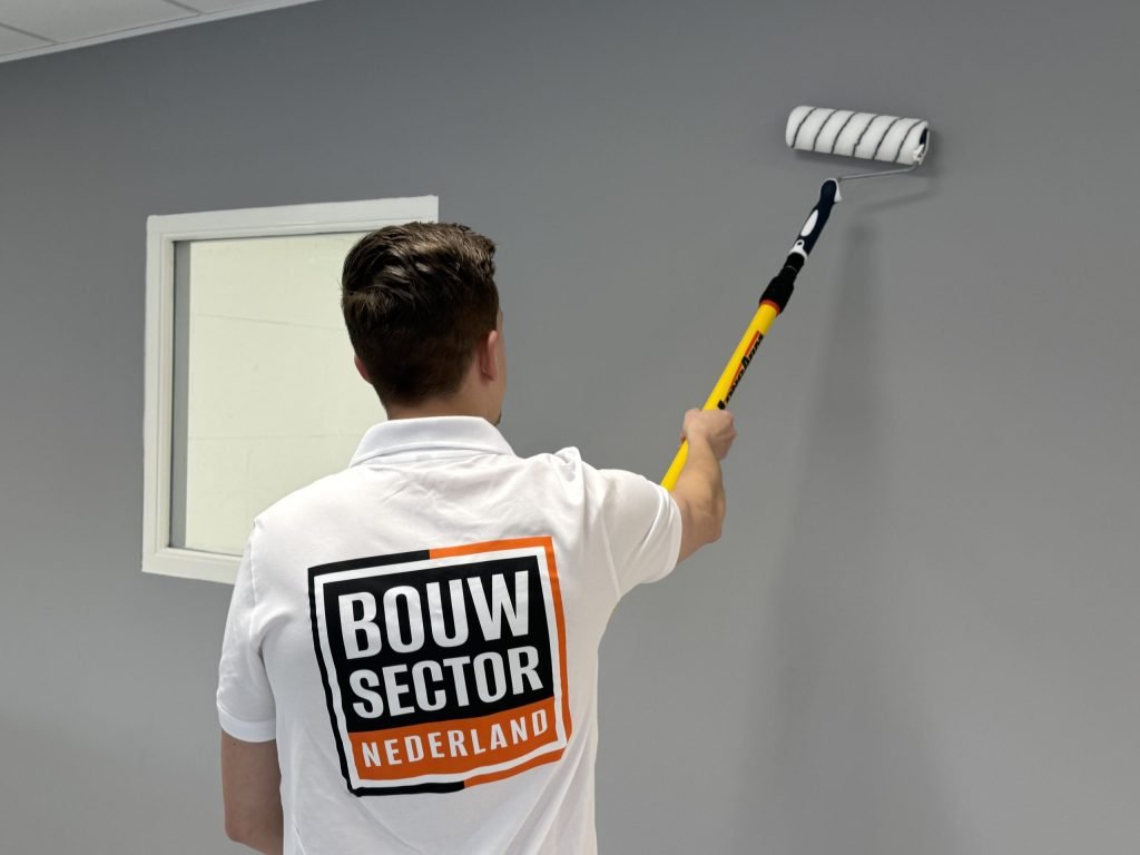 Schilder van Bouwsector Nederland rolt een grijze muur naast een raam met een wit kozijn