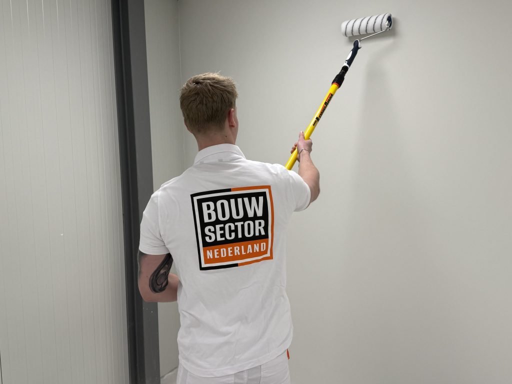 Schilder van Bouwsector Nederland saust een lichte wand in een kamer met de roller op een telescoopsteel