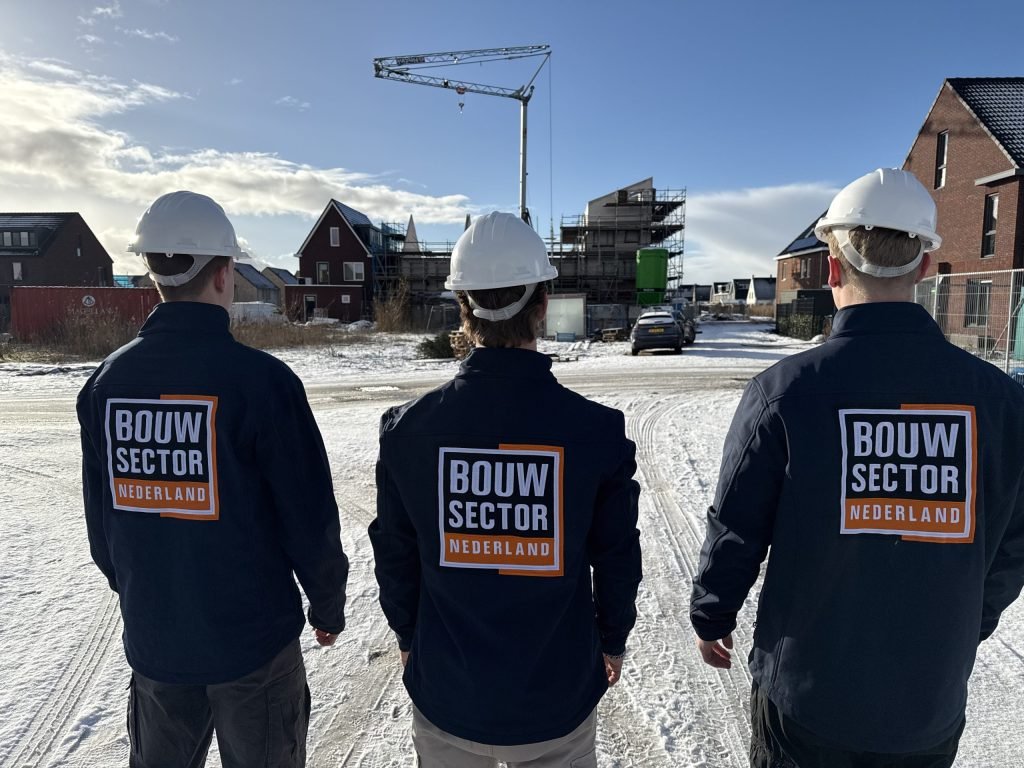 Drie vakmensen van Bouwsector Nederland in donkere jassen met witte helm op een besneeuwde bouwweg