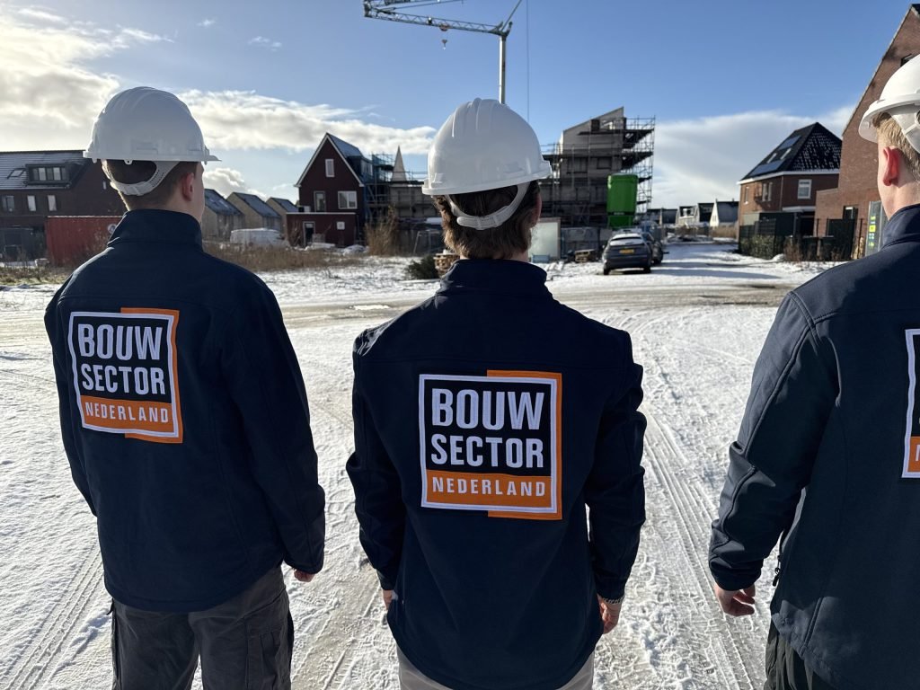 Vakmensen van Bouwsector Nederland met witte bouwhelm en logo op de rug in een besneeuwde straat met nieuwe woningen
